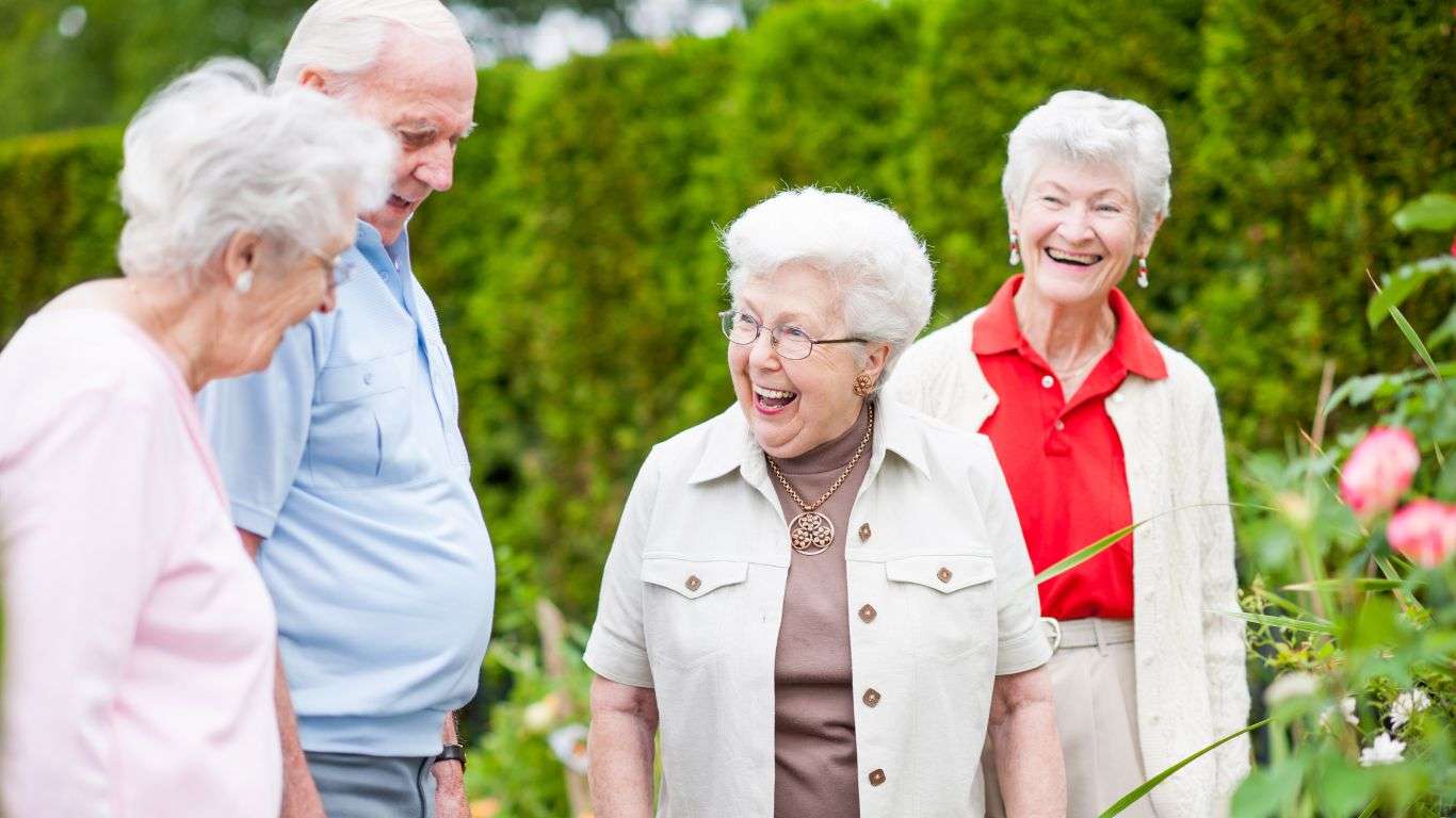 A photo showing a group of elderly people standing in a garden chatting.