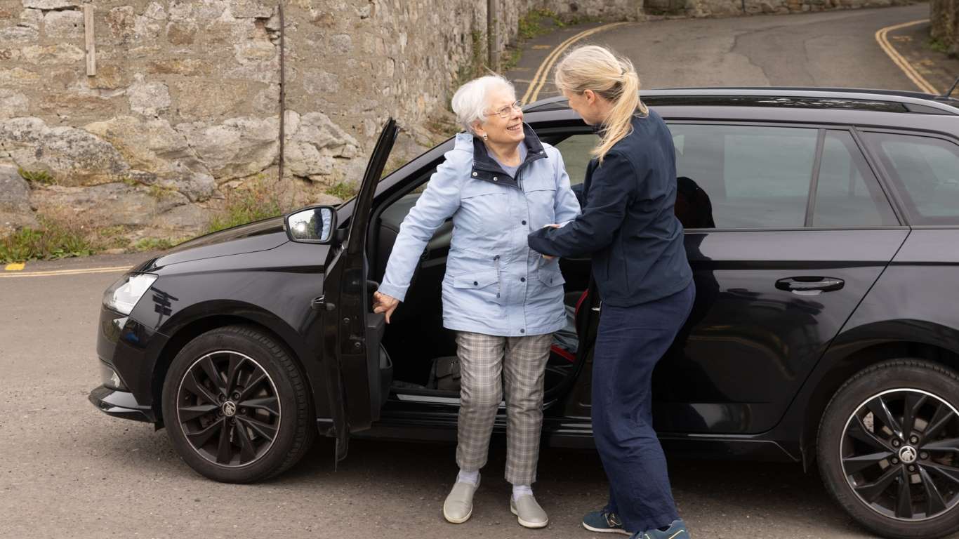 An elderly lady being helped out of the car by a carer.