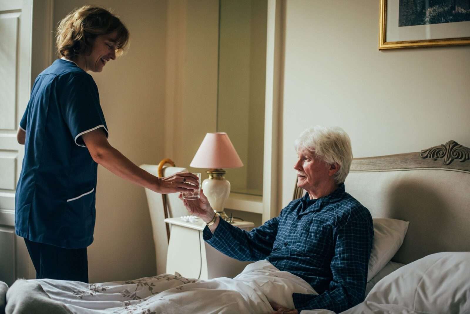 Bright Carer giving water to her client that is sitting in bed