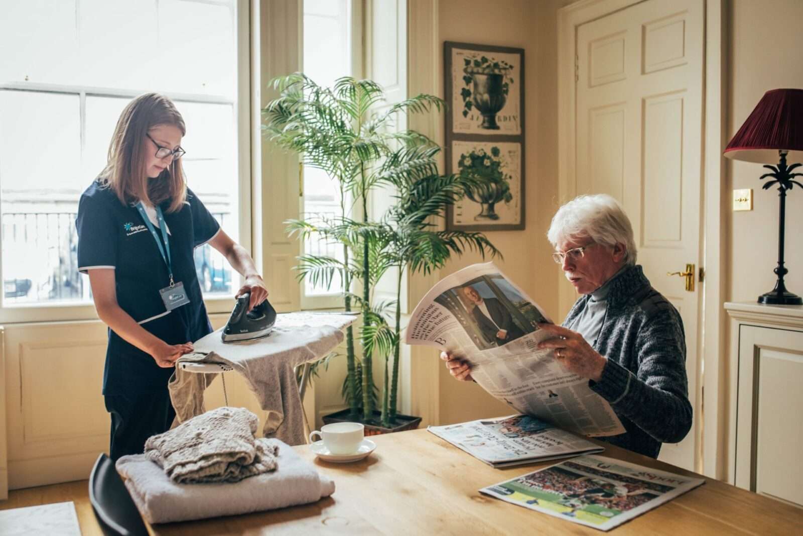 Hourly care, Bright Carer ironing while her client enjoys his newspaper's reading