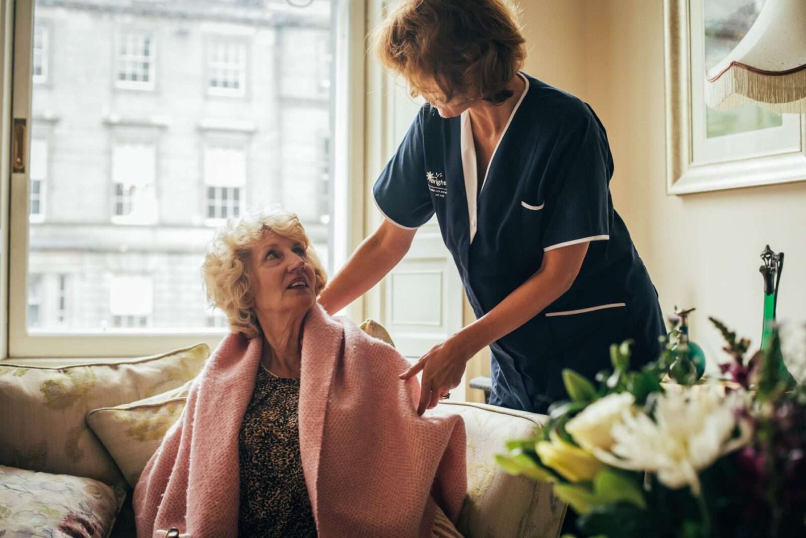 Bright Carer putting blanket on her client' shoulders