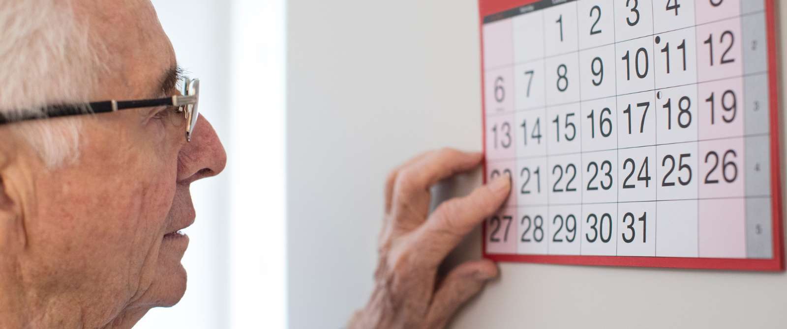 Image of an elder man looking at a wall calendar
