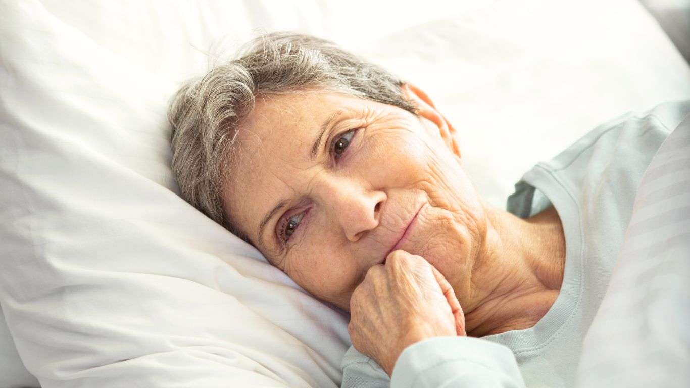 An elderly woman laying down on a white bed.