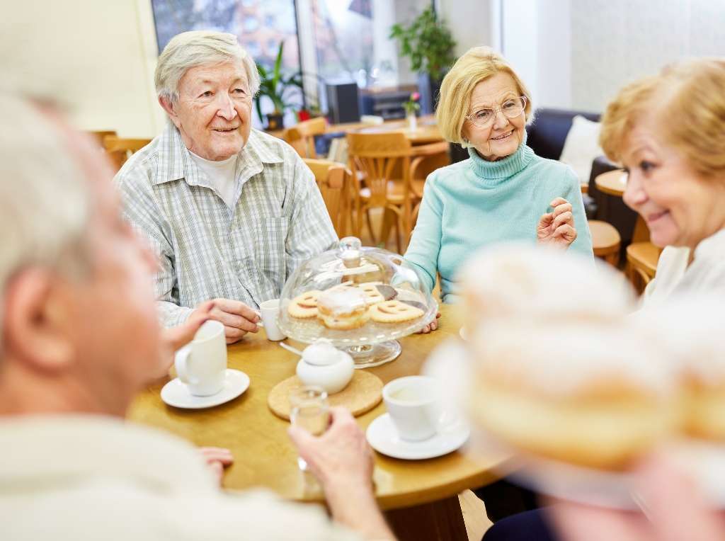 A group of elderly persons enjoying cake and a cuppa.