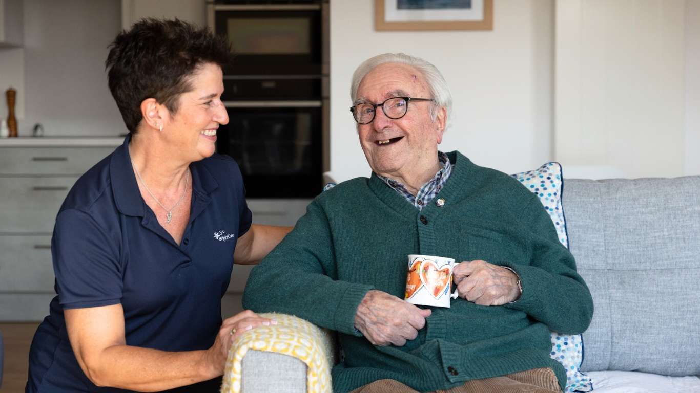 A photo showing an elderly gentleman laughing with the company of a Bright Care carer.