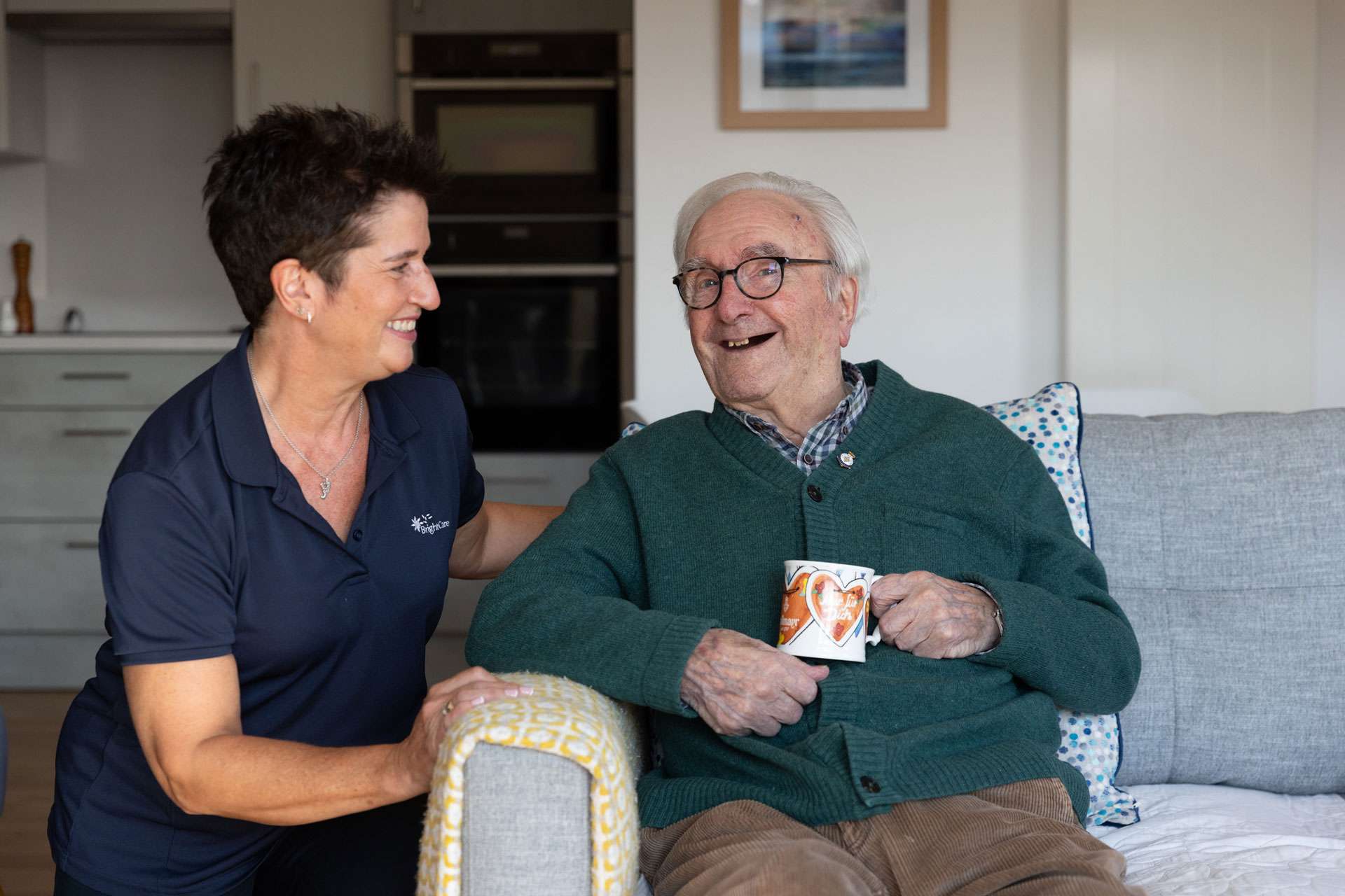 A photo showing an elderly gentleman laughing with the company of a Bright Care carer.